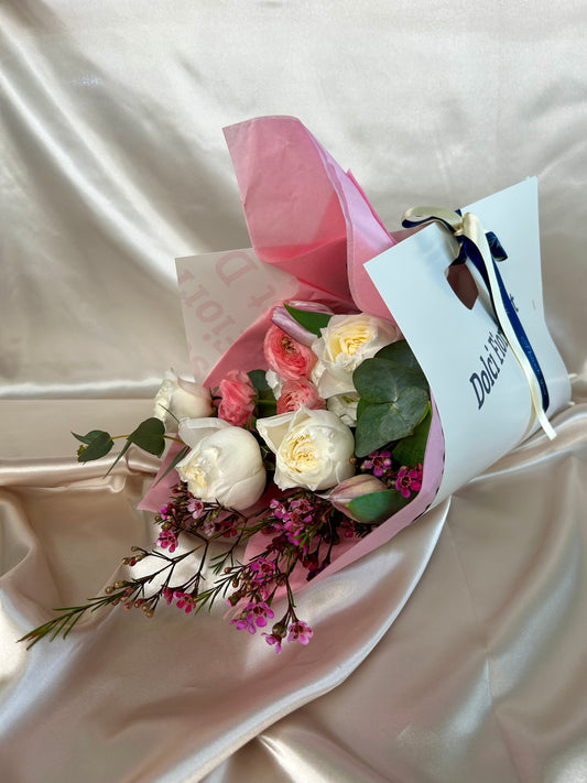A white rose Dolci Fiori Florist bouquet wrapped in pink paper and sitting in a paper bag.